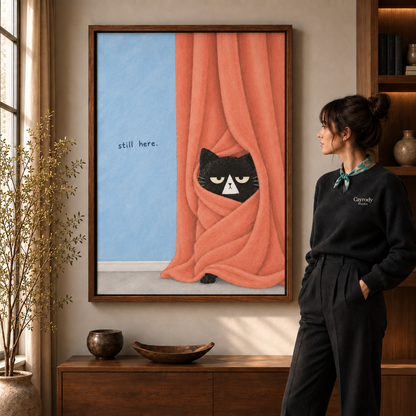 Woman in a black sweater viewing a framed black cat peeking from peach curtains artwork in a warm living room.