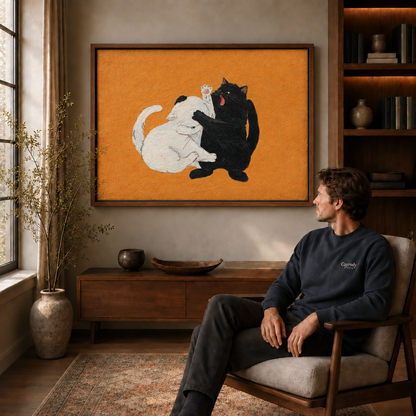 Black and white cats play-fighting in framed canvas wall art above a wooden console near a window.