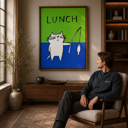 Man seated in an armchair beside a walnut floating-frame wall art of a white cat fishing with LUNCH above.