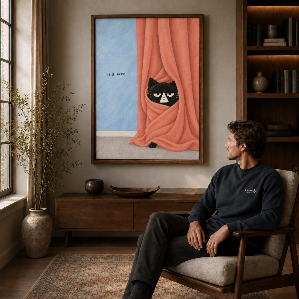 Man seated in an armchair beside a walnut floating-frame wall art of a black cat peeking from peach curtains.