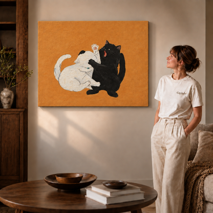 Play-fighting black and white cats on canvas displayed beside a woman in white and a coffee table.