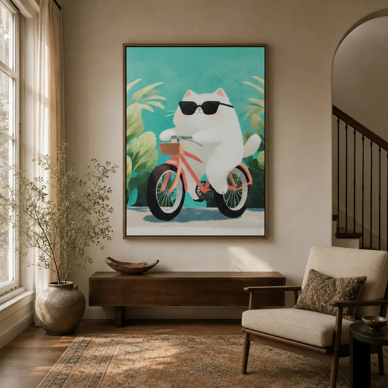 Framed canvas of a chubby white cat in sunglasses riding a pink bicycle, displayed in a bright entryway
