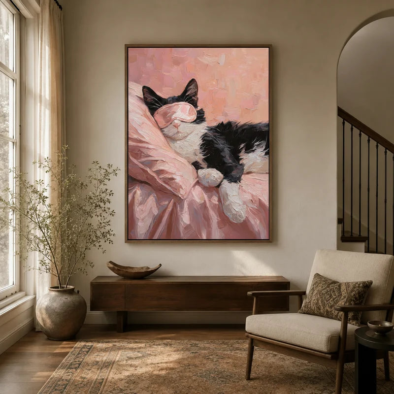 Framed sleeping cat with pink eye mask canvas wall art hung in a warm neutral hallway