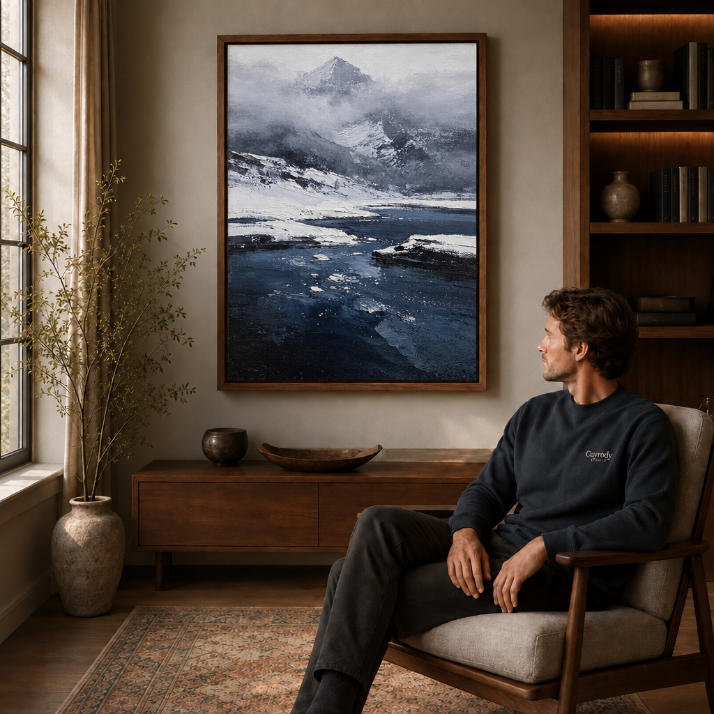 Framed snowy mountain lake wall art styled beside a seated man in a cozy study