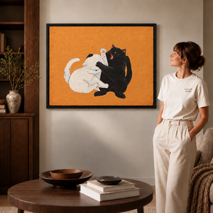 Play-fighting cats canvas wall art on an orange background above a cabinet beside a seated man.