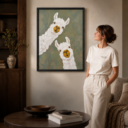 Alpaca canvas wall art in a black frame above a coffee table with shelving, sofa, and standing woman.