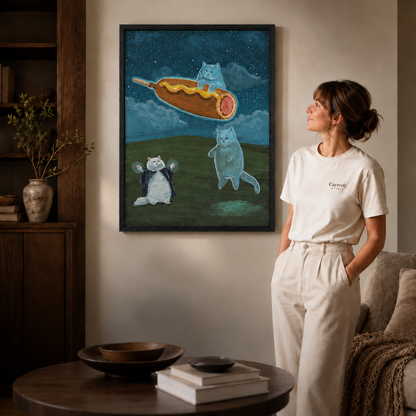 A slim black framed surreal cat wall art piece of a caped cat and flying corn dog hangs in a warm living room.