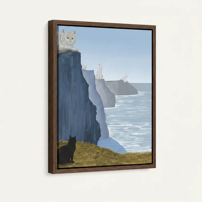 Side-angle view of dark-framed canvas showing black cat at cliff base with white cats perched on layered sea cliffs