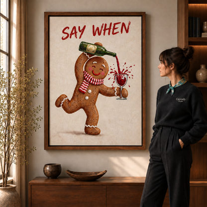 Framed Say When gingerbread wine canvas above a wooden console, viewed by a woman in a black sweater.