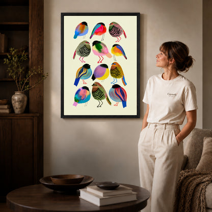 Colorful birds canvas art in a black frame above stacked books in a cozy living room.