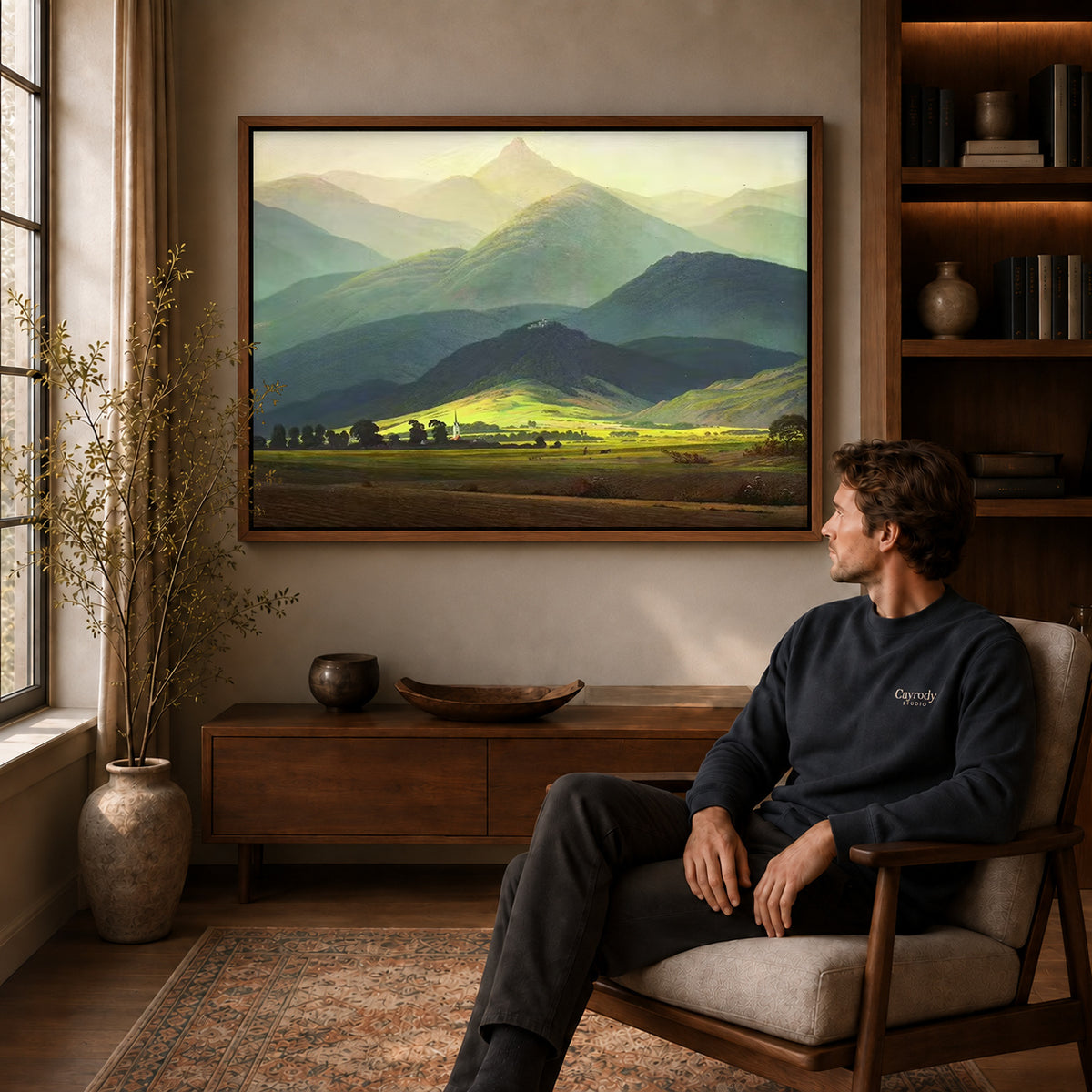 Mountain valley canvas art above a wooden console near a seated man and leafy branches.