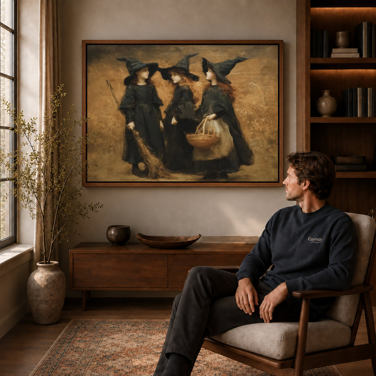 Three witches canvas art above a wooden console near a seated man and leafy branches.
