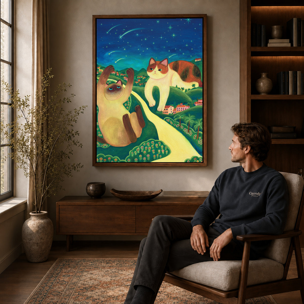 Starry cats canvas art above a wooden console near a seated man and leafy branches.