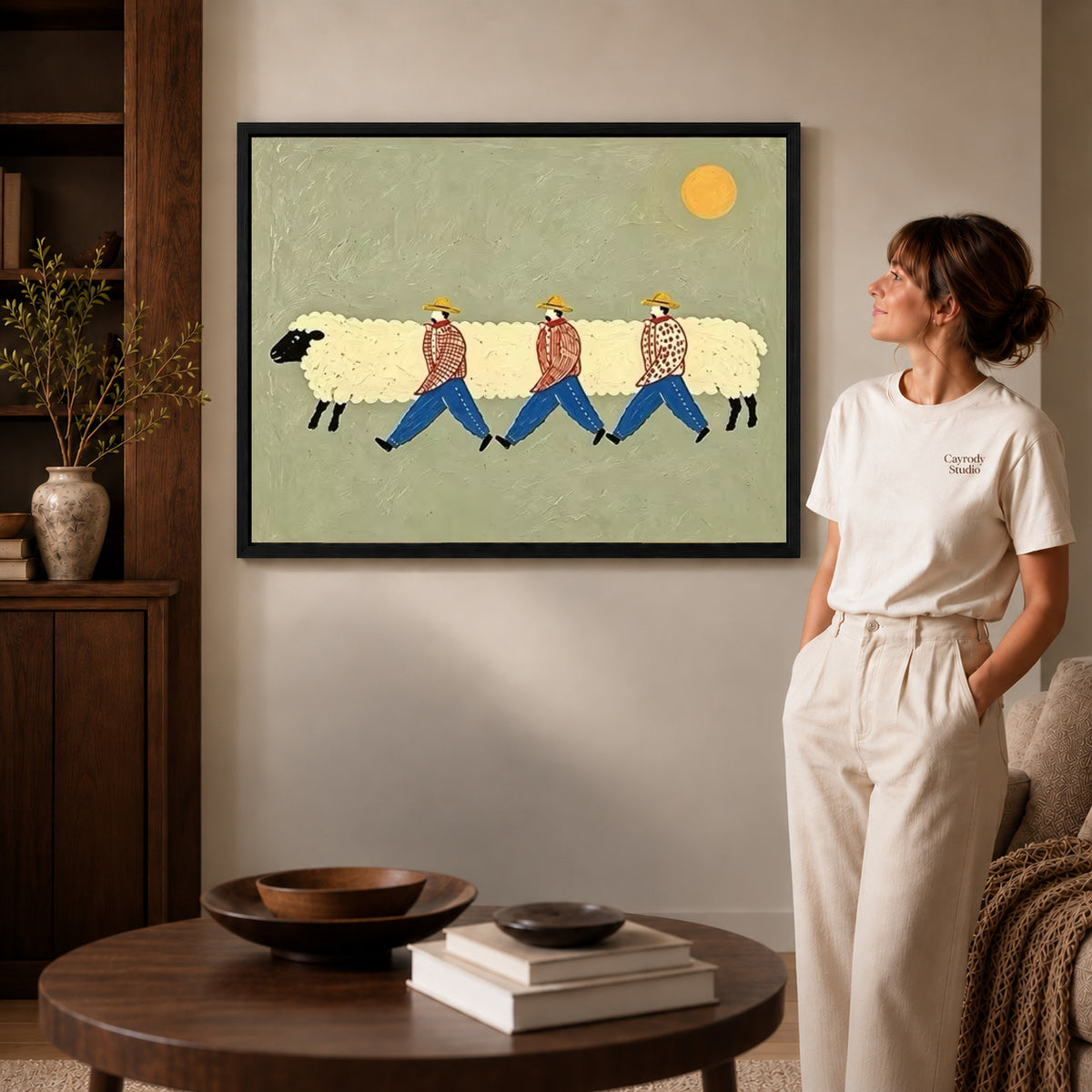 Sheep parade canvas art in a black frame above stacked books in a cozy living room.