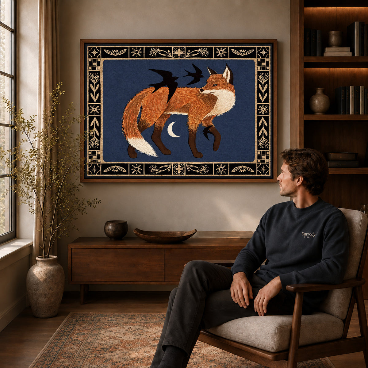 Fox and birds canvas art above a wooden console near a seated man and leafy branches.
