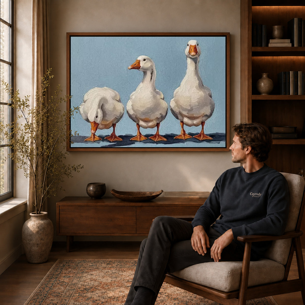Three geese canvas art above a wooden console near a seated man and leafy branches.