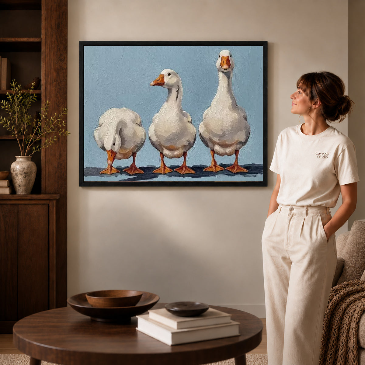Three geese canvas art displayed in a black frame beside a woman, with soft room lighting.