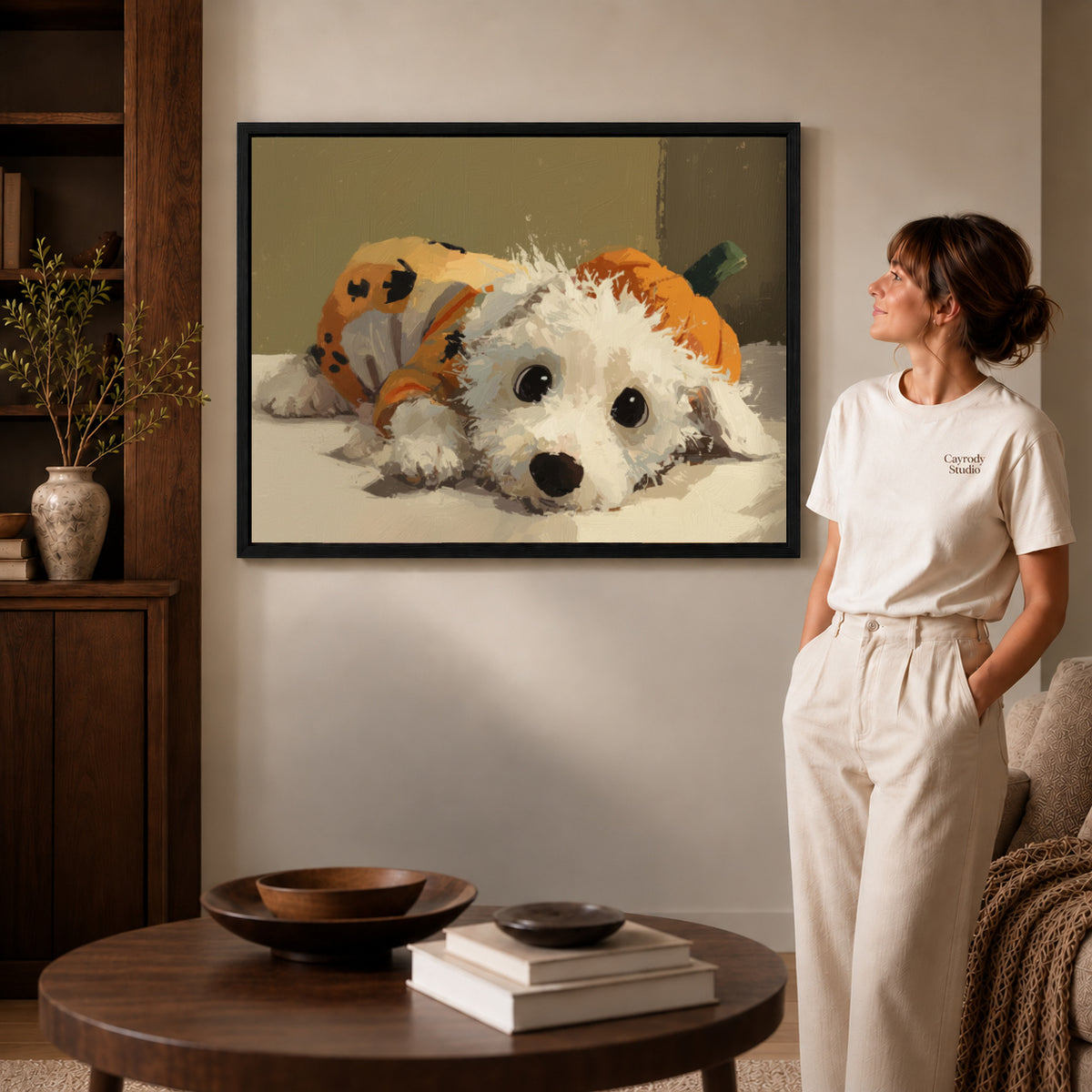 Pumpkin puppy canvas art in a black frame above stacked books in a cozy living room.
