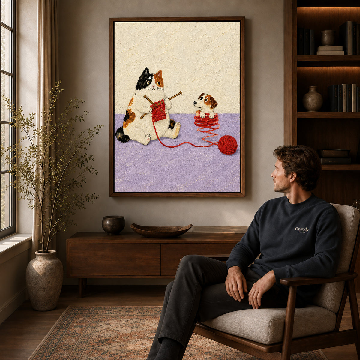 Knitting Cat canvas art above a wooden console beside a seated man in a warm room.