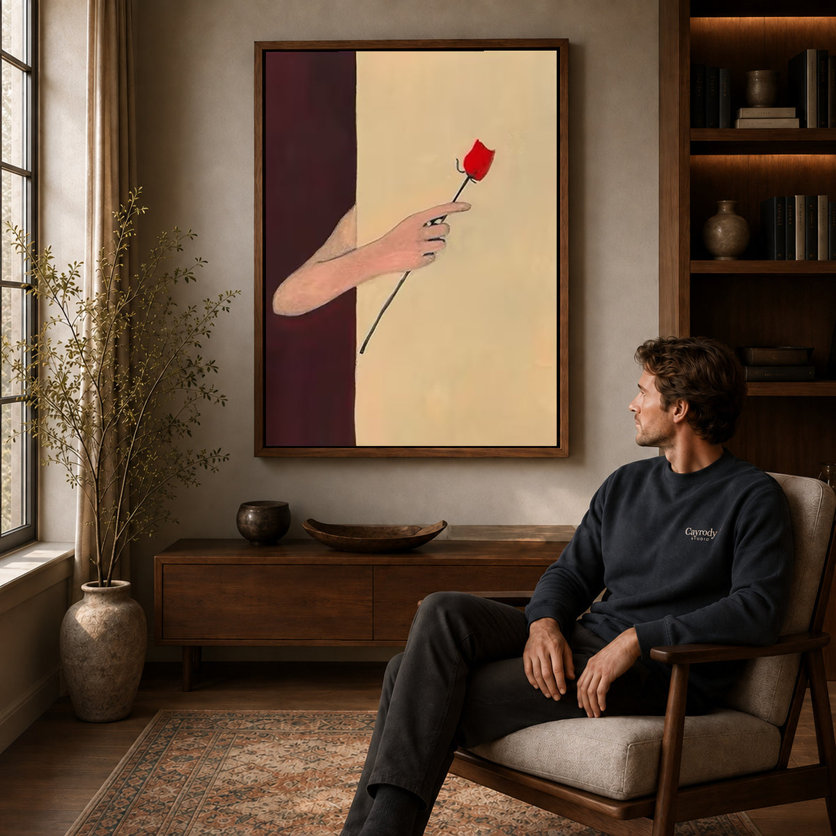 Red rose canvas art above a wooden console near a seated man and leafy branches.
