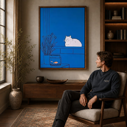 Blue cat canvas art above a wooden console near a seated man and leafy branches.