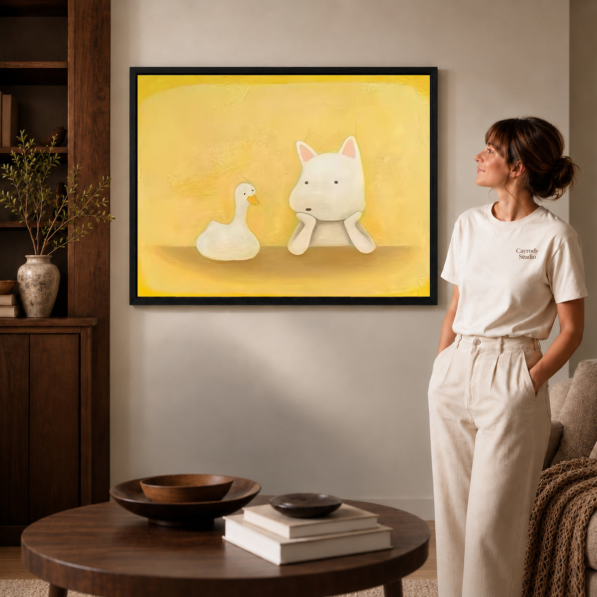 Dog and duck canvas art in a black frame above stacked books in a cozy living room.