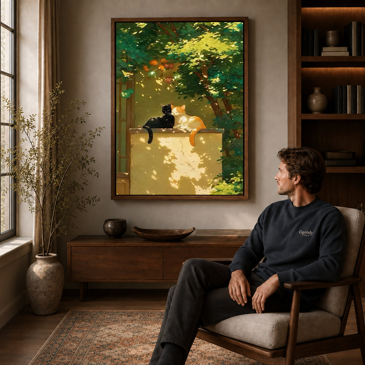 Garden cats canvas art above a wooden console near a seated man and leafy branches.