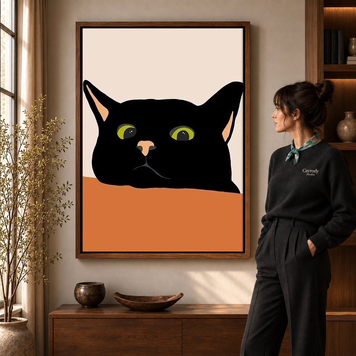 Black cat canvas art in a walnut frame beside a woman in a warmly lit living room.