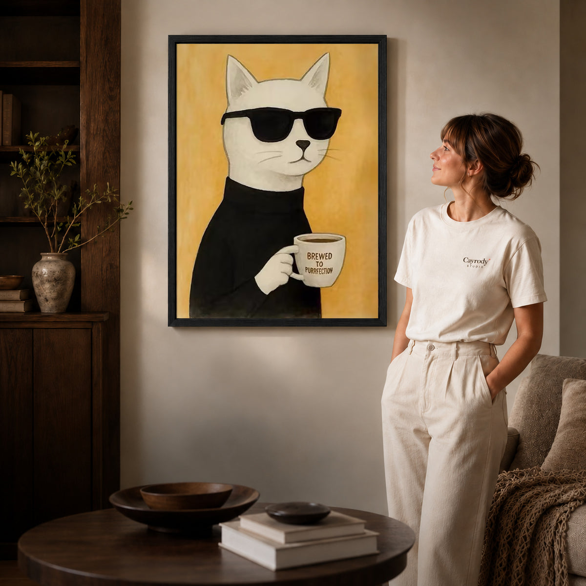 Coffee cat canvas art in a black frame above stacked books in a cozy living room.
