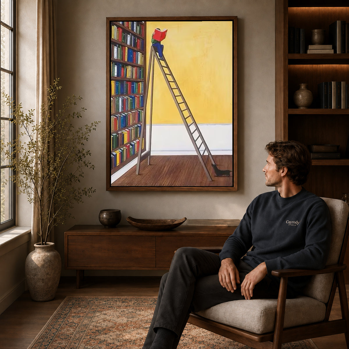 Library reader canvas art above a wooden console near a seated man and leafy branches.