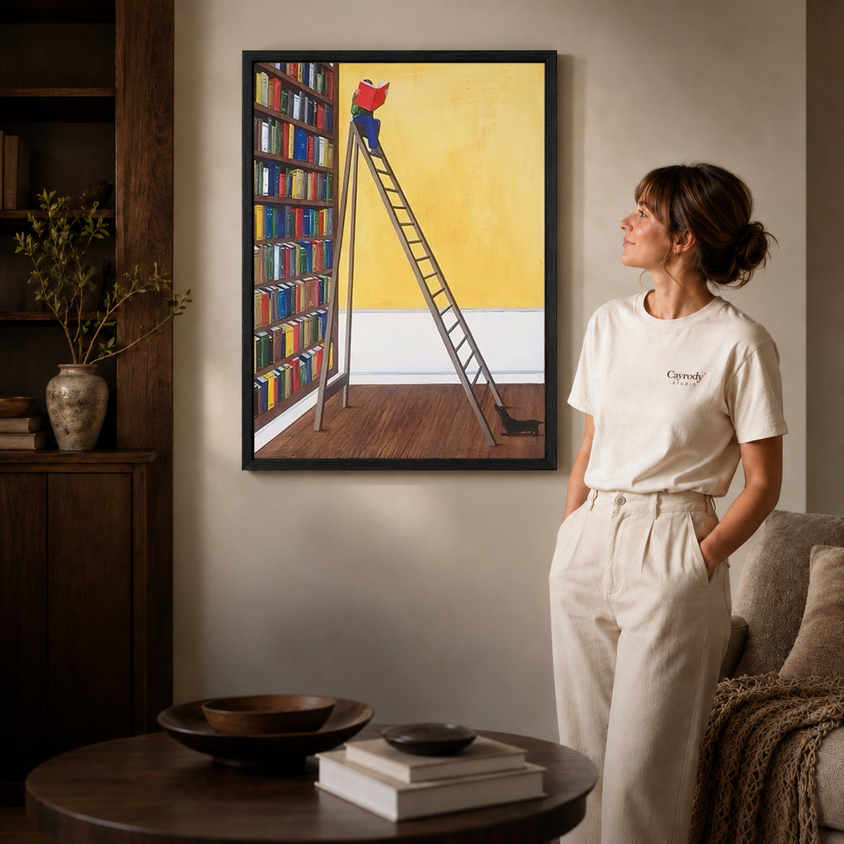 Library reader canvas art in a black frame above stacked books in a cozy living room.