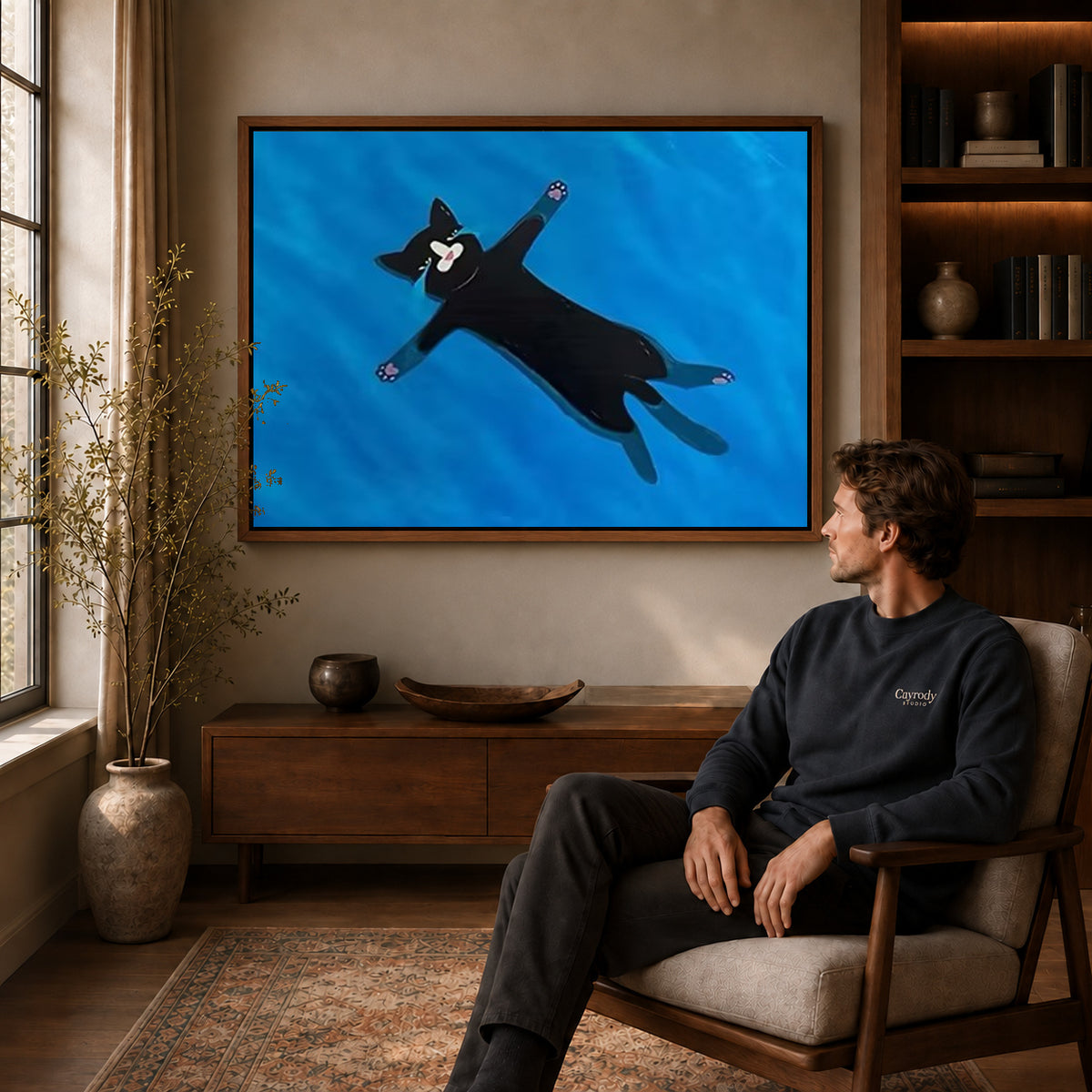 Floating black cat canvas art above a wooden console near a seated man and leafy branches.