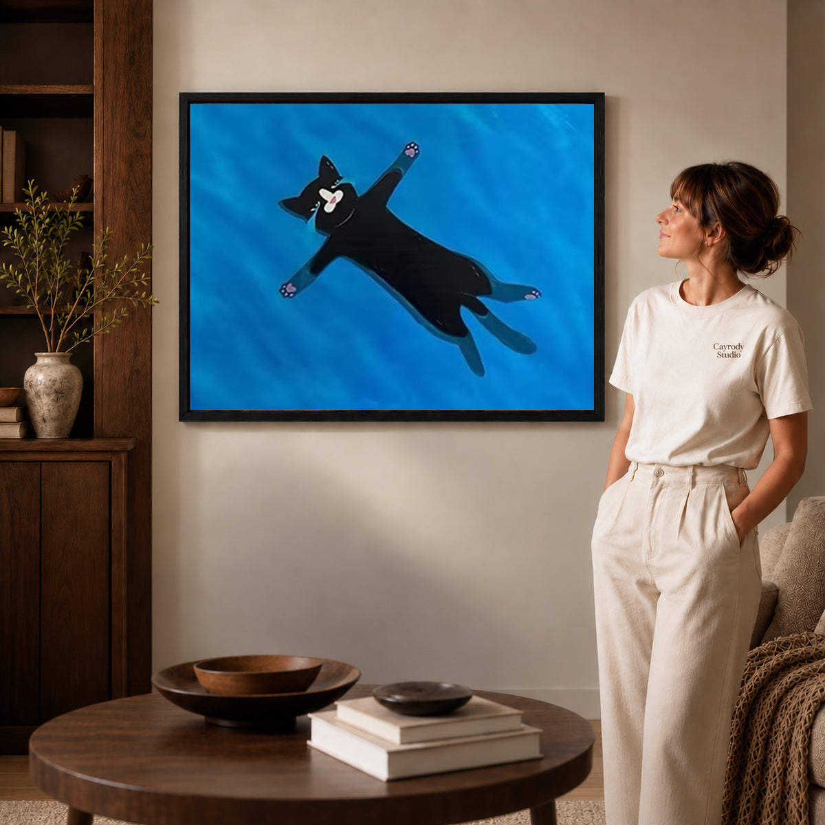 Floating black cat canvas art displayed in a black frame beside a woman, with soft room lighting.