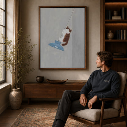 Pendant cat canvas art above a wooden console near a seated man and leafy branches.