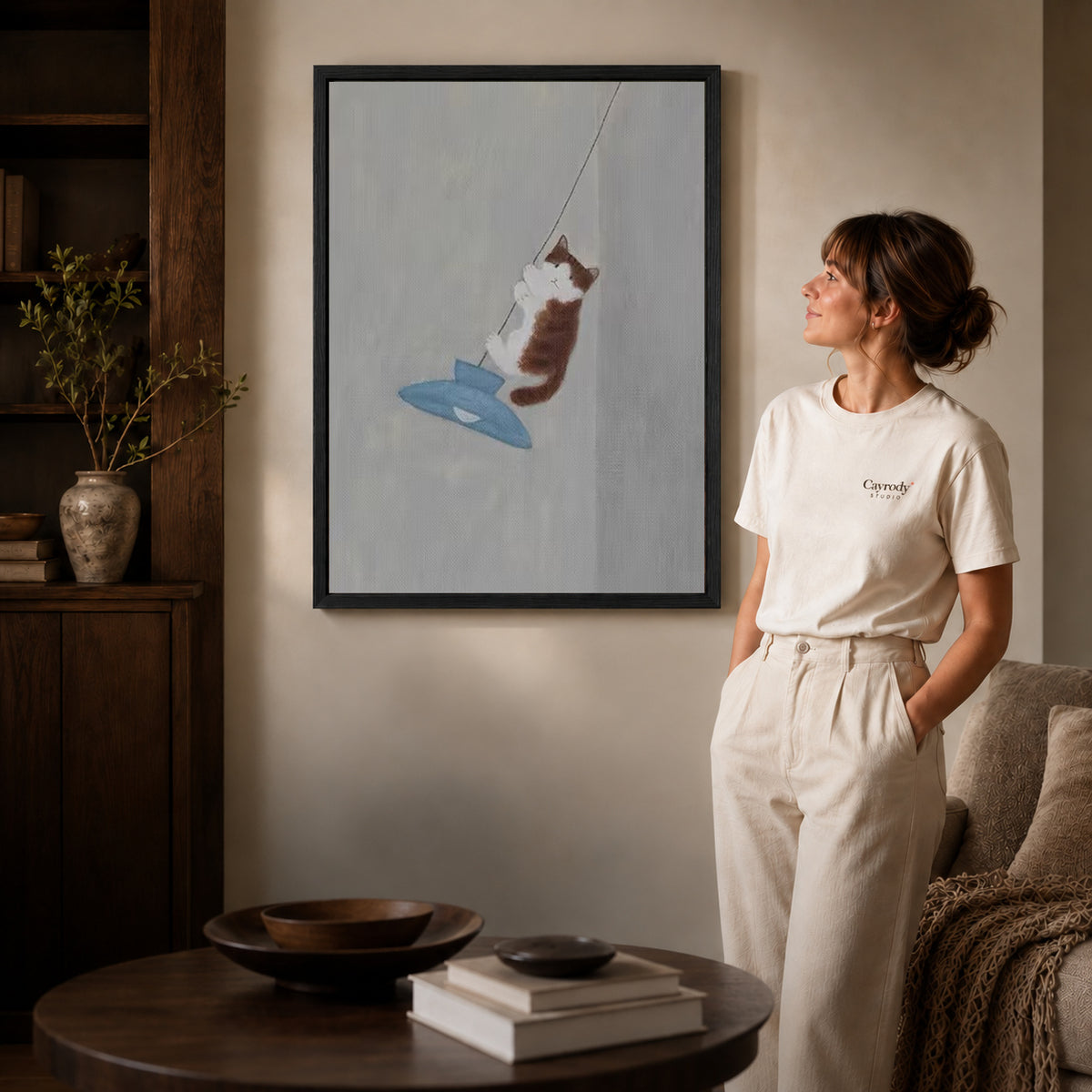 Pendant cat canvas art displayed in a black frame beside a woman, with soft room lighting.
