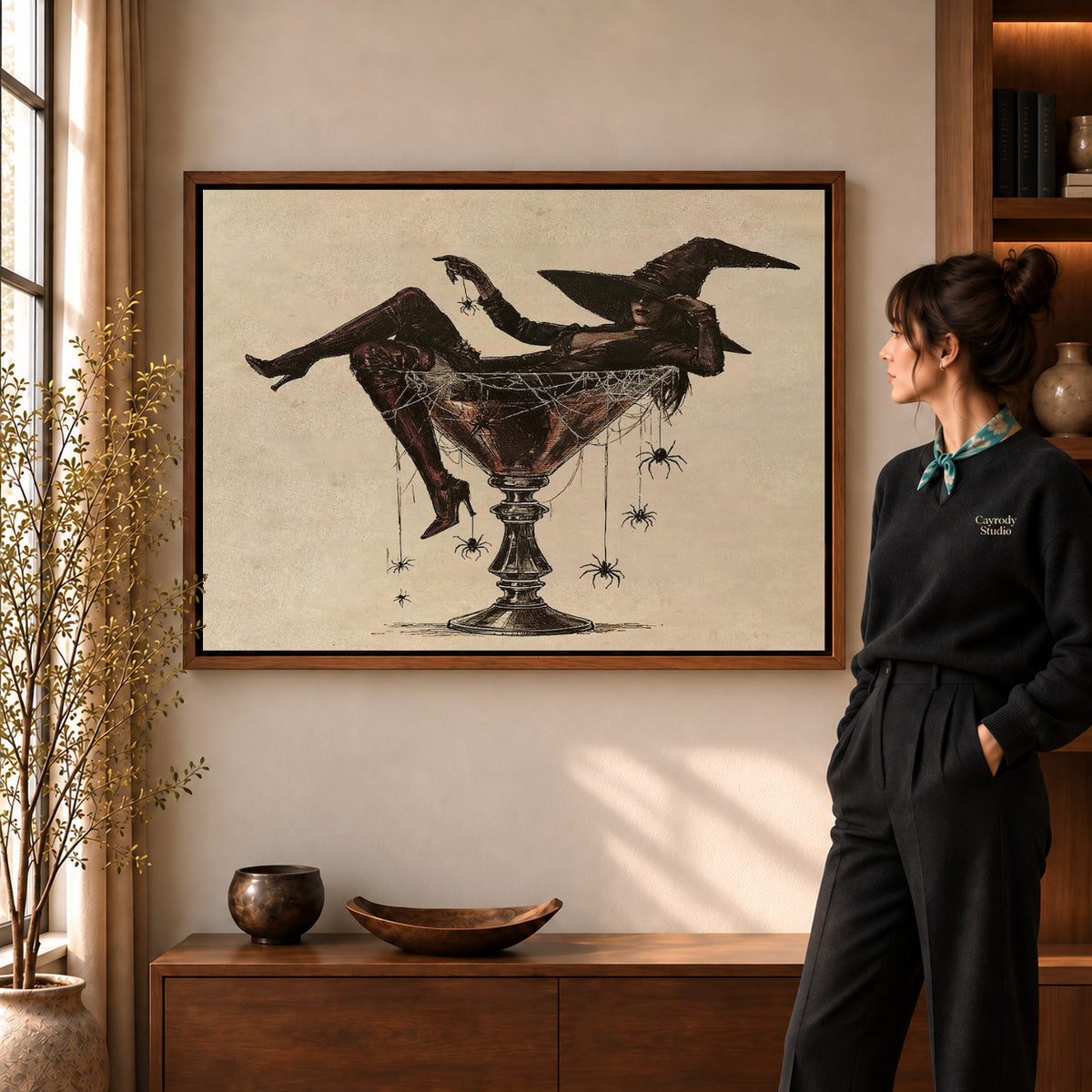 Martini Witch canvas art in a walnut frame beside a standing woman and wooden console.