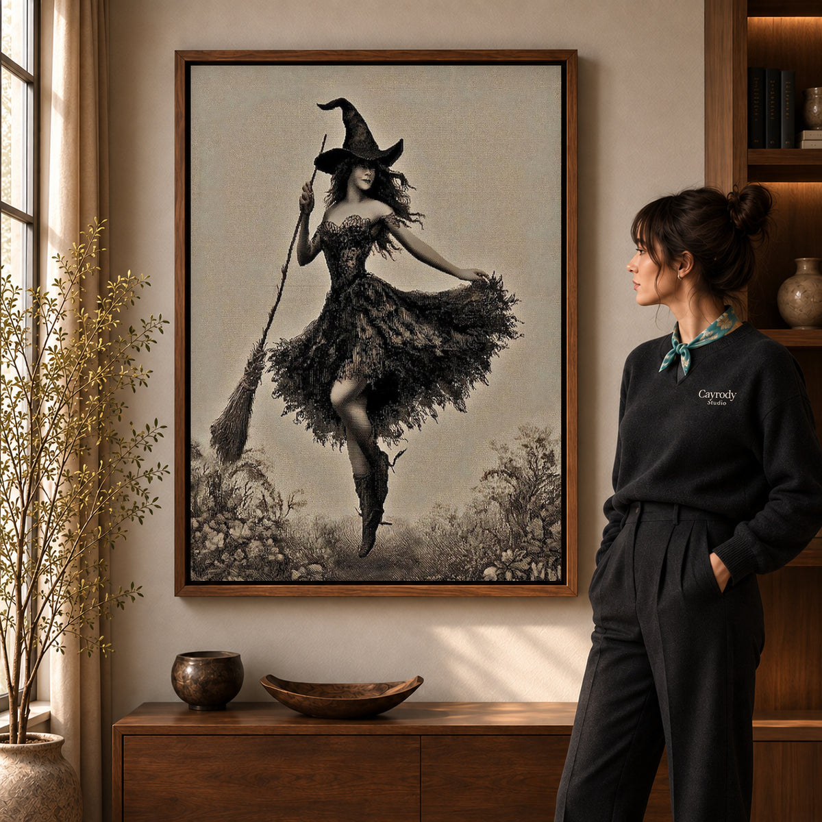 Walnut framed dancing witch canvas art shown beside a standing woman and a wooden console.