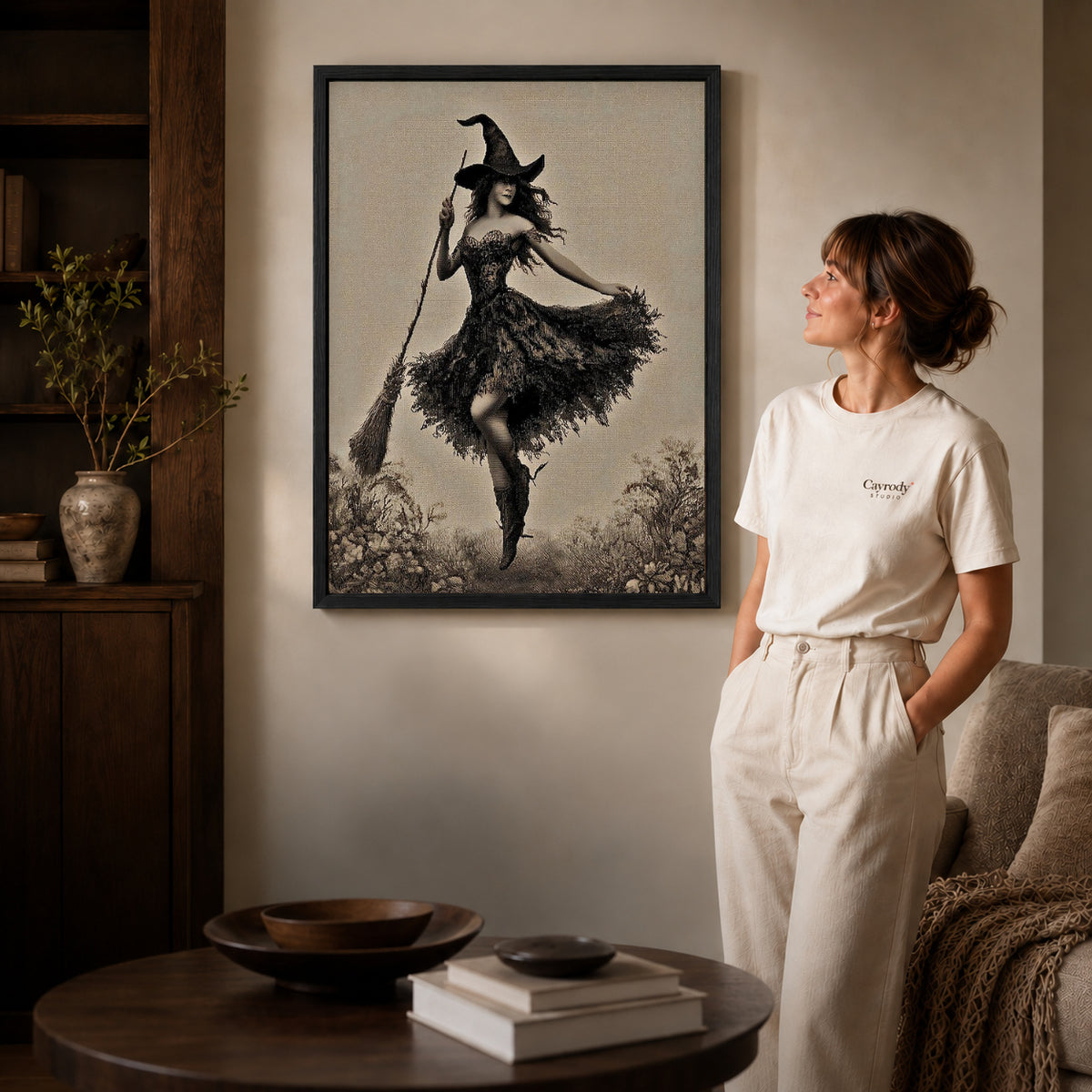 Black framed dancing witch canvas art displayed beside a woman in a warm living room.