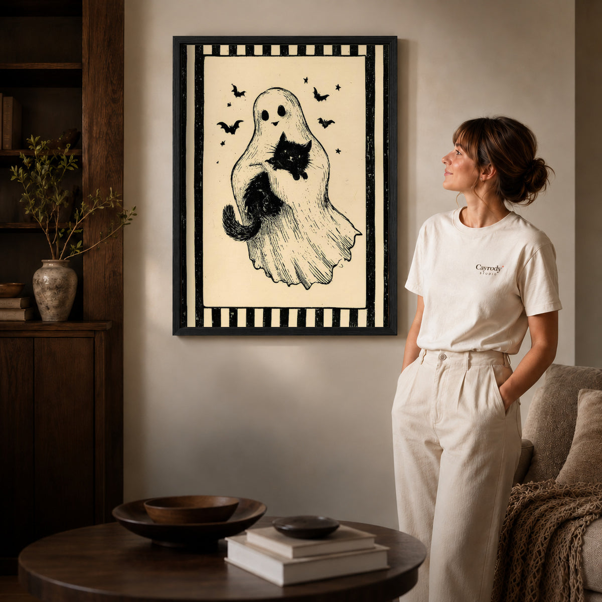 Ghost And Cat canvas art in a black frame above books in a welcoming living room.