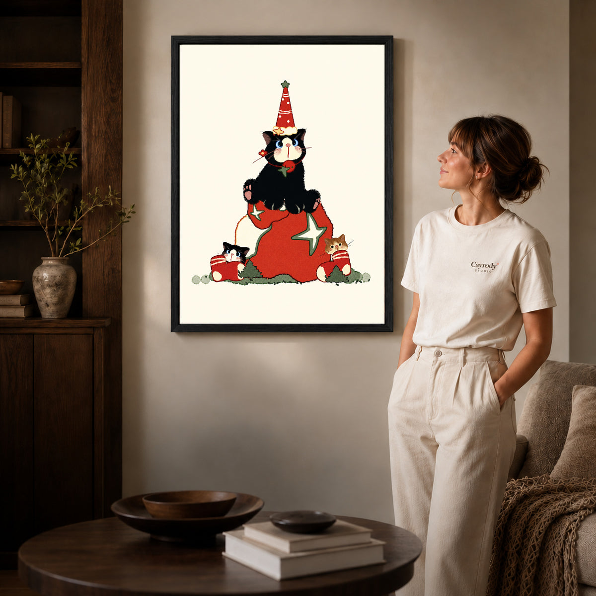 Black framed christmas kittens canvas art displayed beside a woman in a warm living room.