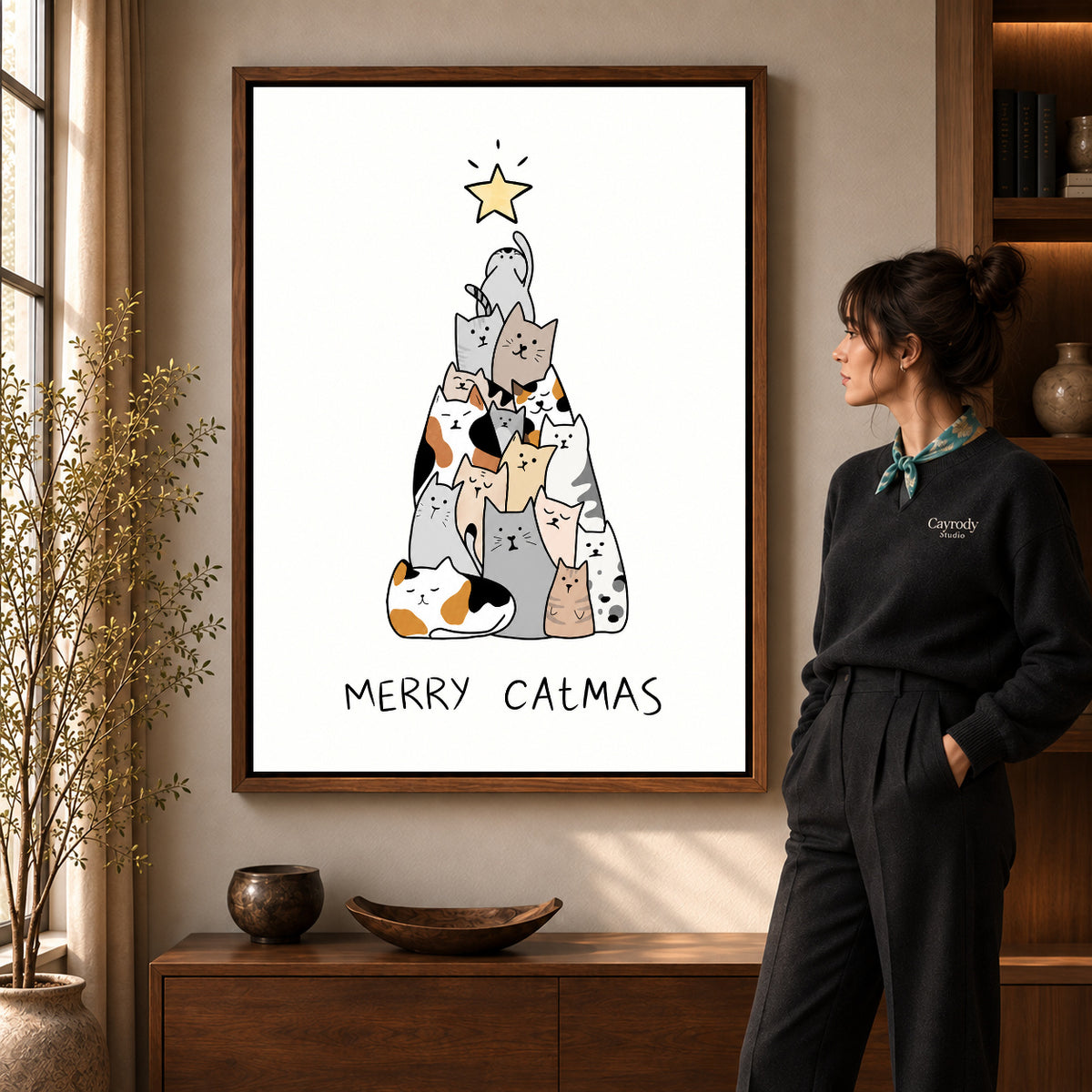 Cat Christmas canvas art in a walnut frame beside a standing woman and wooden console.