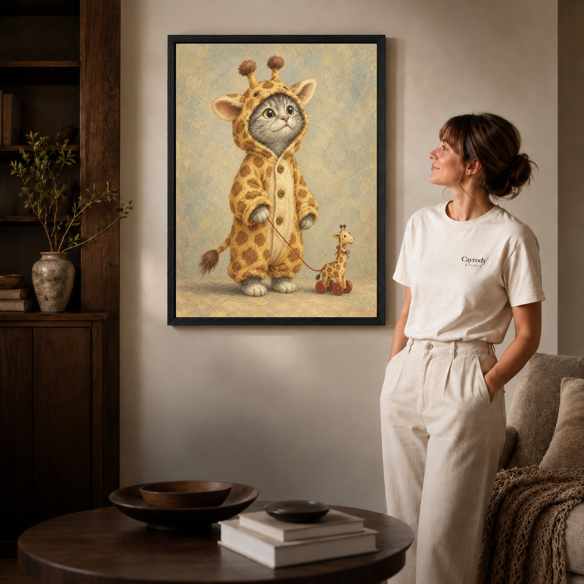 Black framed giraffe kitten canvas art displayed beside a woman in a warm living room.