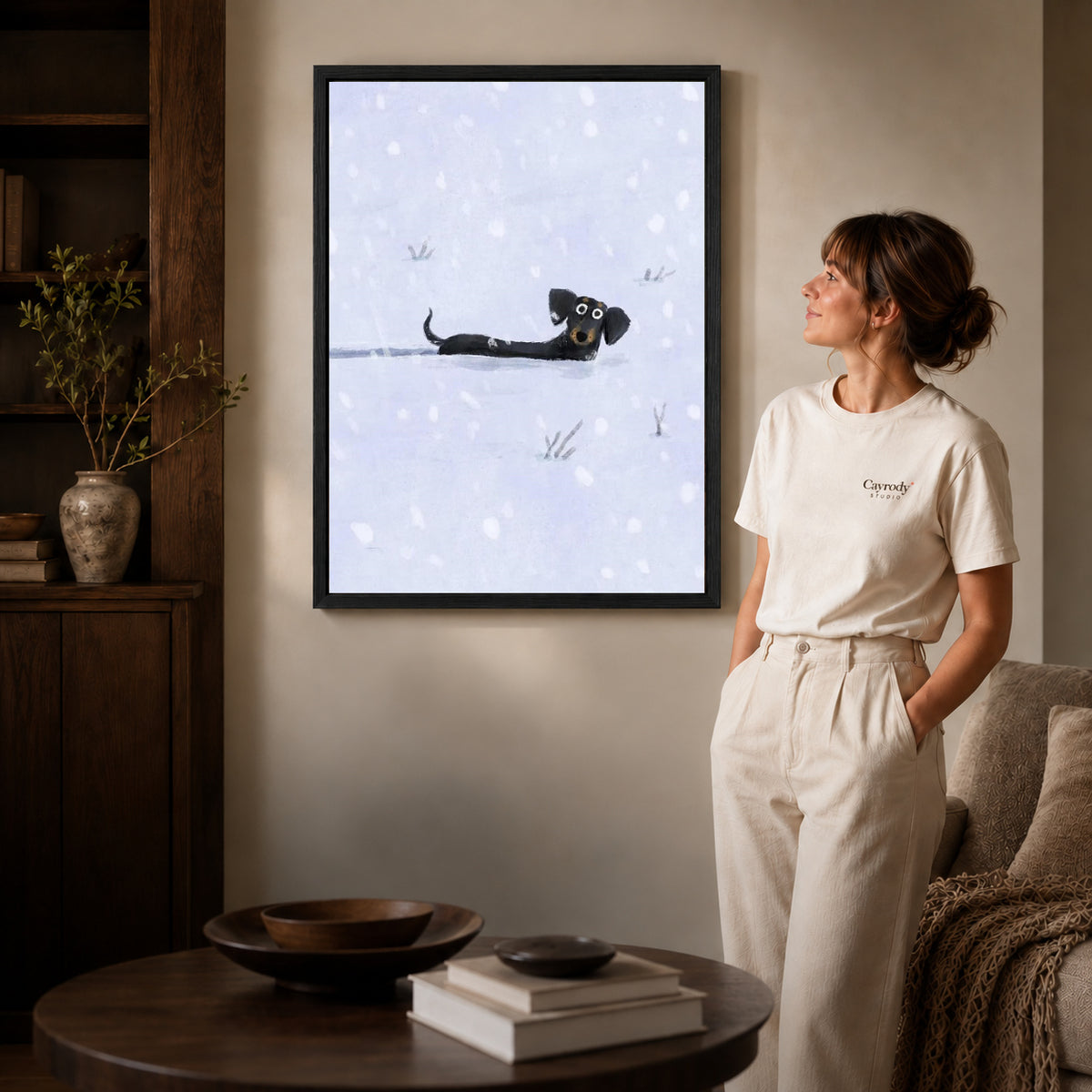 Black framed snowy dachshund canvas art displayed beside a woman in a warm living room.