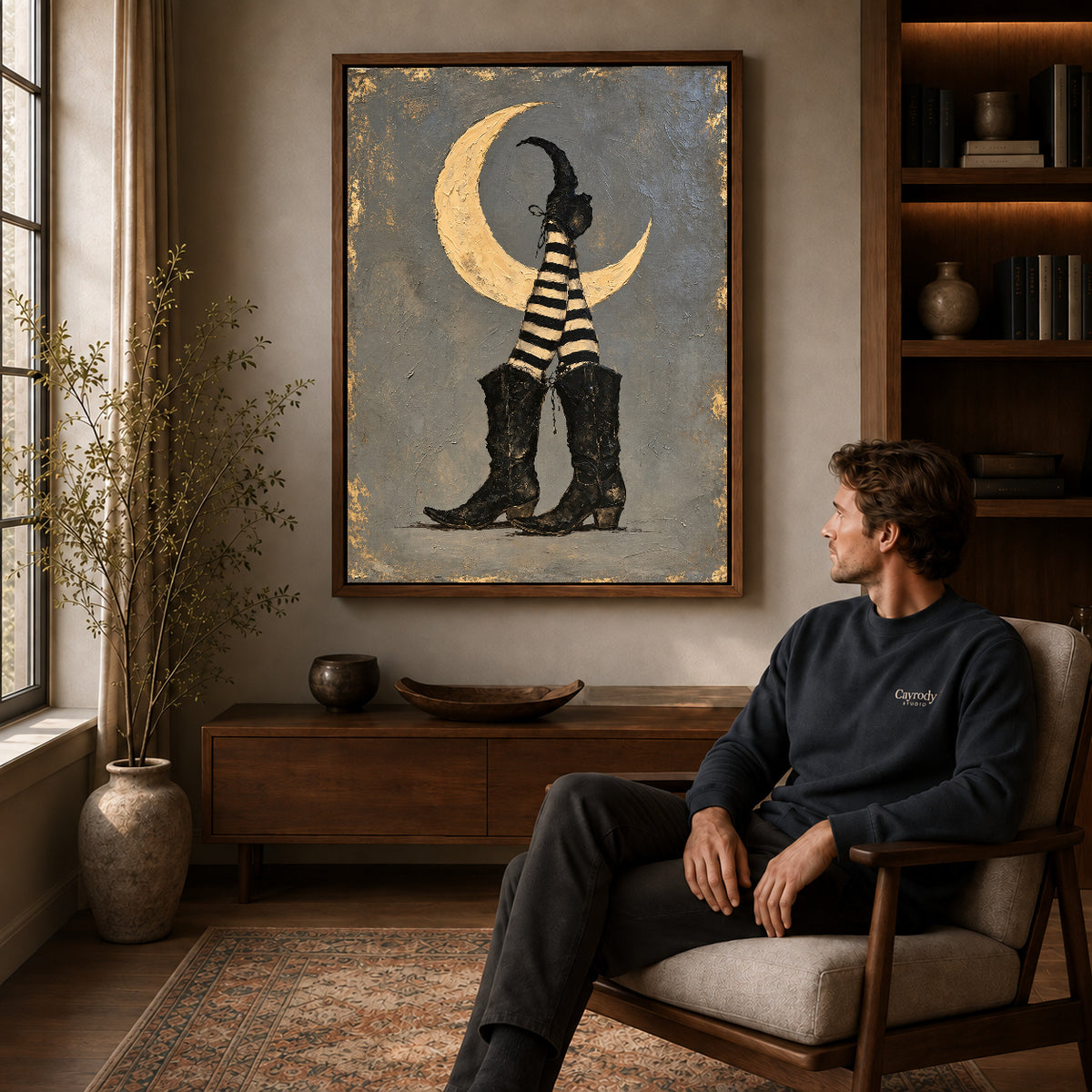 Moonlit Witch Boots canvas art above a wooden console beside a seated man in a warm room.