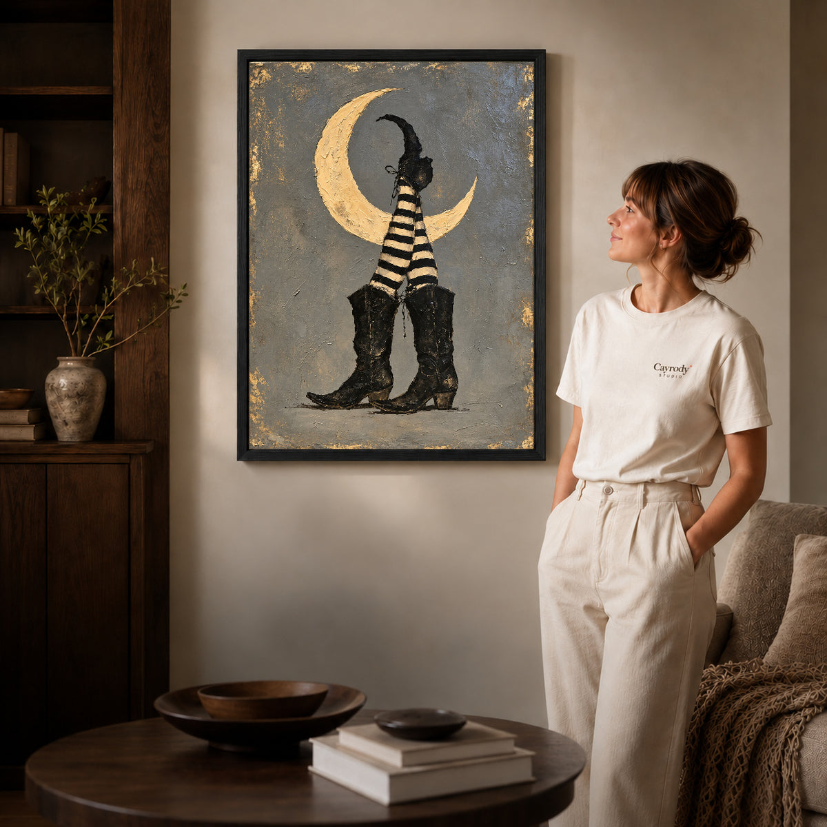Black framed moonlit witch boots canvas art displayed beside a woman in a warm living room.