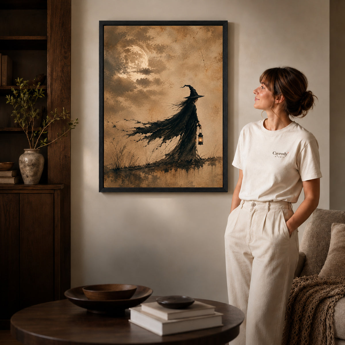 Black framed lantern witch canvas art displayed beside a woman in a warm living room.