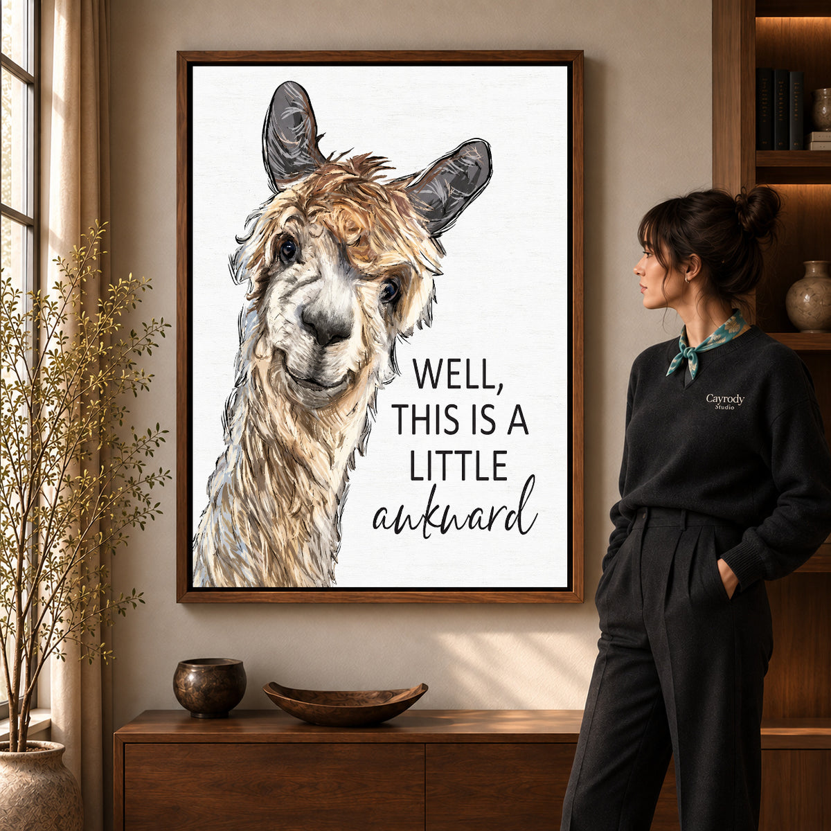 Awkward Alpaca canvas art in a walnut frame beside a standing woman and wooden console.