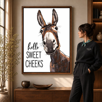 Sweet Cheeks Donkey canvas art in a walnut frame beside a standing woman and wooden console.