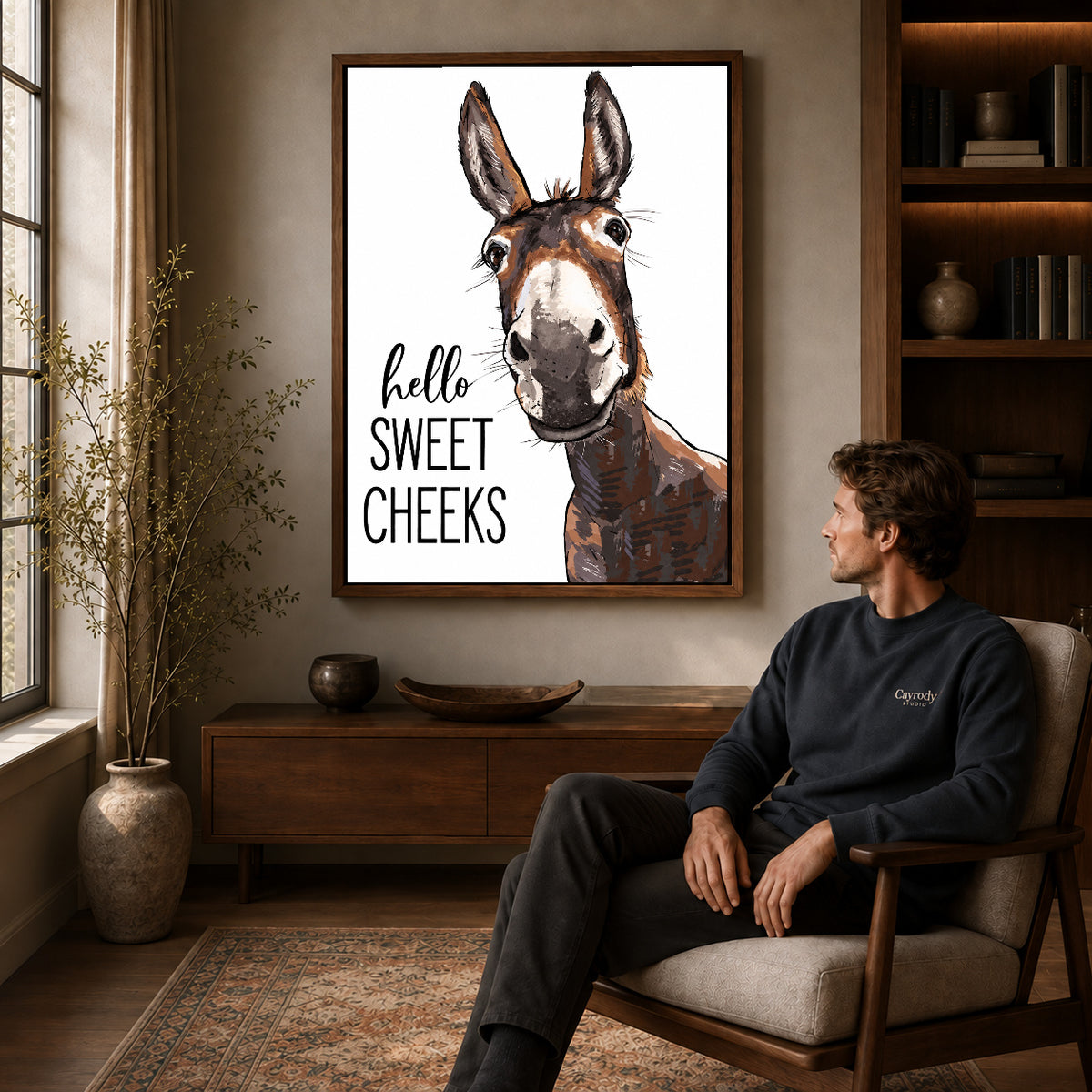 Sweet Cheeks Donkey canvas art above a wooden console beside a seated man in a warm room.