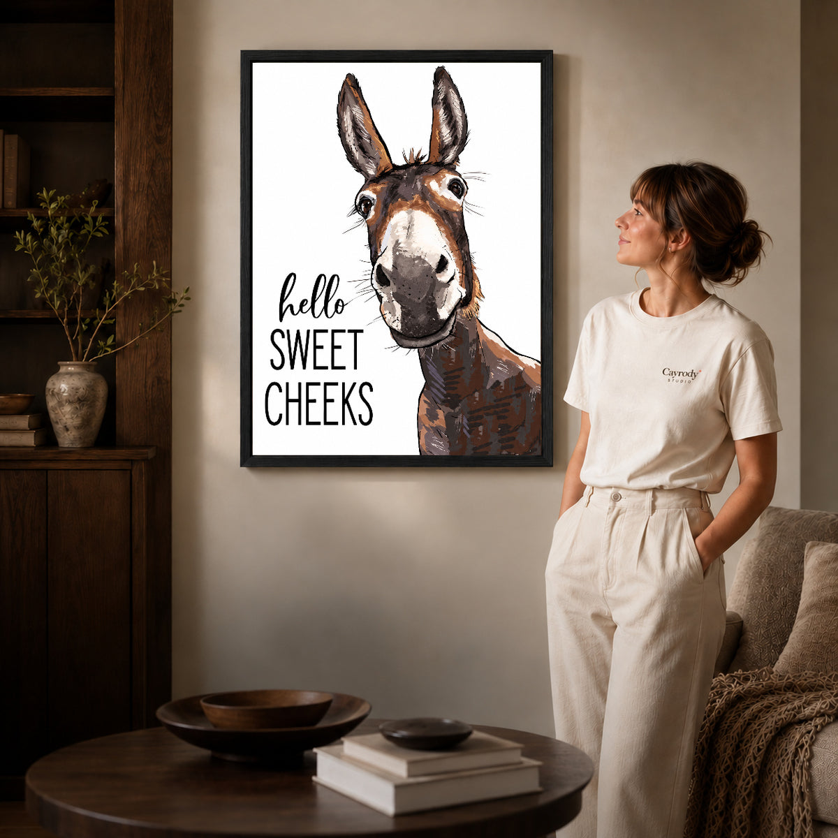 Sweet Cheeks Donkey canvas art in a black frame above books in a welcoming living room.
